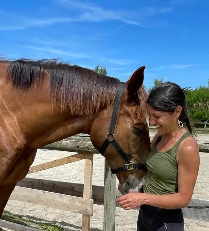 Massages et soins - Portrait de Laura avec un cheval bai dans un paysage ensoleillé sous un ciel bleu.